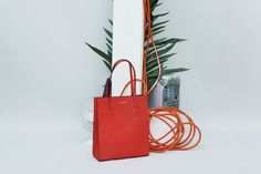 a red bag sitting next to a tall white column with plants and other items on it