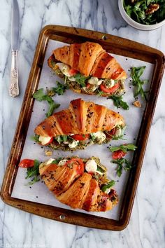 four slices of chicken wrapped in bread and garnished with lettuce on a tray next to a bowl of salad