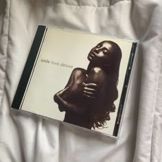 a cd case sitting on top of a bed covered in white sheets and blankets, with the cover pulled back