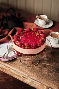 a cake with strawberries on top sits on a table next to two cups and saucers