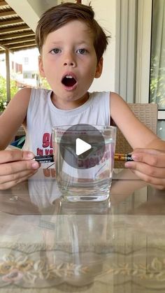 a little boy sitting at a table with a glass in front of him and his mouth open