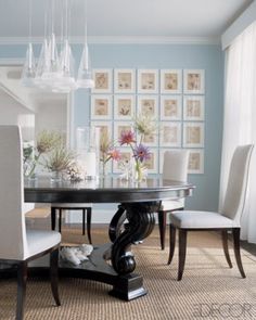 a dining room table with white chairs and pictures on the wall behind it, along with a chandelier