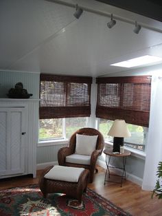 a chair and ottoman in a small room with two windows that have blinds on them