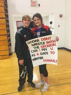 two people standing in a gym holding a sign that says, godart don't wrestle with decision can i pin u as a date to winter formal?