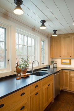 a kitchen with wooden cabinets and black counter tops next to two large windows that look out onto the yard