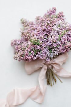 a bouquet of purple flowers wrapped in a pink ribbon on a white surface with a bow around it