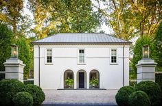 a white house surrounded by trees and bushes in the middle of a driveway with an entry way leading to it