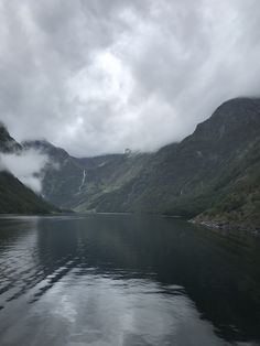 the mountains are covered in fog and clouds as they sit on top of a body of water