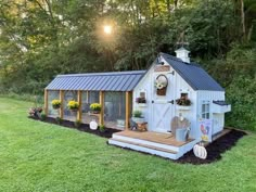 a small white shed with windows and flowers on the front porch is surrounded by green grass