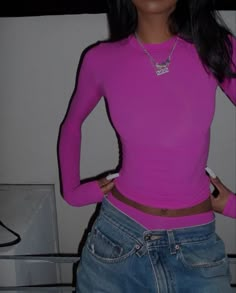 a woman in a pink shirt and jeans is posing for the camera with her hands on her hips