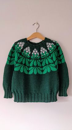 a green sweater with white flowers is hanging on a wooden hanger and it's attached to a wall