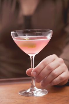 a person holding a wine glass with pink liquid in it on top of a wooden table