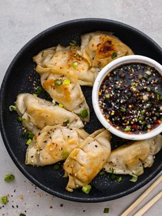 a black plate topped with dumplings next to chopsticks and a bowl of dipping sauce