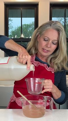 a woman pouring liquid into a blender on top of a counter