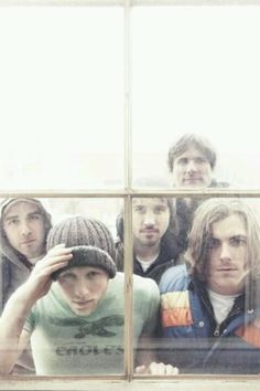 four young men looking through a window at the camera while one man holds his head in his hands