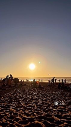 people are on the beach as the sun sets over the ocean and sand is covering them