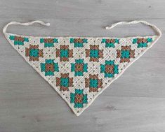 a crocheted triangle is hanging on a wooden surface with white string and green accents