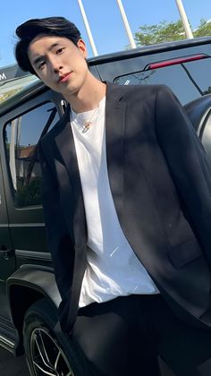 a young man standing next to a car wearing a black suit and white t - shirt