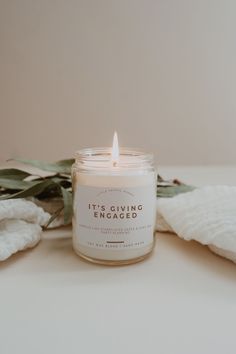 a candle sitting on top of a table next to some white towels and eucalyptus leaves