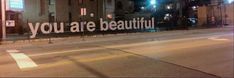 an empty street at night with the words you are beautiful written in large white letters