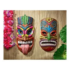 three masks are hanging on the wall next to some pink and green flowers in front of them