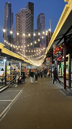 many people are walking down the street in front of some tall buildings at night time