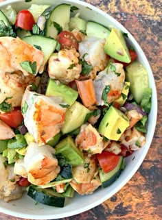 a white bowl filled with shrimp, avocado and tomato salad on top of a wooden table