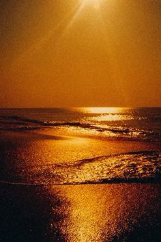 the sun shines brightly over the ocean on a beach at night with waves lapping in front of it