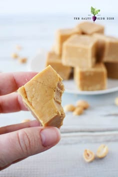 a hand holding a peanut butter fudge in front of a plate full of peanuts