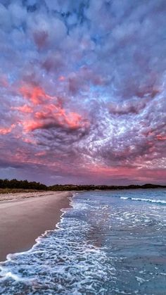 an ocean beach with waves coming in to shore and colorful clouds above it at sunset