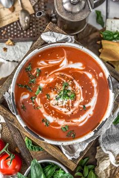 a bowl of tomato soup on a wooden cutting board with basil and tomatoes in the background