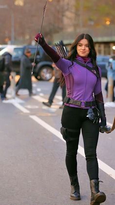 a woman dressed in black and purple is holding an arrow while walking down the street