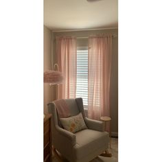 a living room with a chair, lamp and window covered in pink drapes on the windowsill