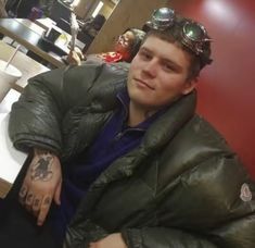 a man wearing goggles sitting in a booth at a restaurant with his arm tattooed