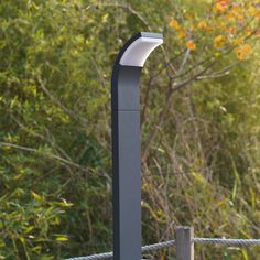 a metal pole with a light on top of it next to some grass and trees