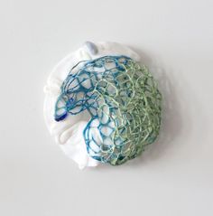 a piece of art made out of yarn on top of a white surface with blue and green swirls