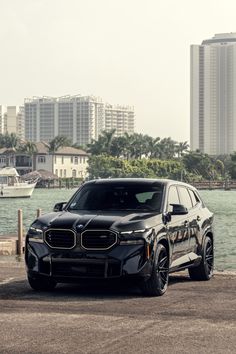 a black bmw suv parked in front of a body of water with buildings in the background