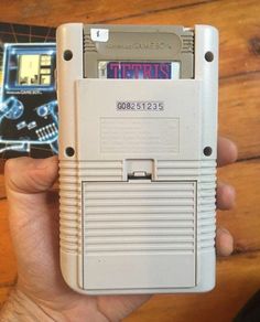 a hand holding an old nintendo gameboy in front of a wooden table