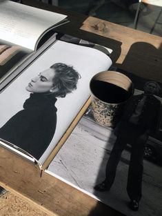 an open book sitting on top of a wooden table next to a coffee cup and magazine