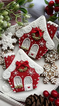 two gingerbread houses decorated with red and white icing on a plate next to christmas decorations