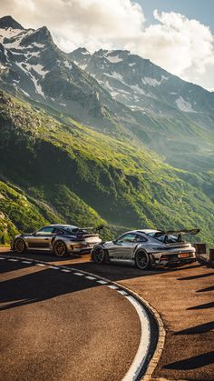 three sports cars parked on the side of a road in front of a mountain range