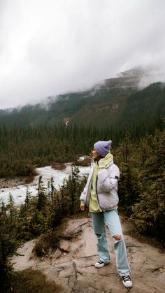 a woman standing on top of a rock next to a forest