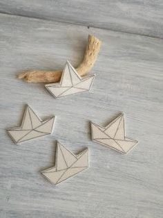 four origami birds sitting on top of a white wooden table next to a piece of driftwood