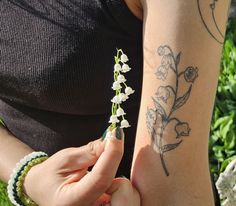 a woman is holding a small white flower in her right hand and the other arm has tattoos on it