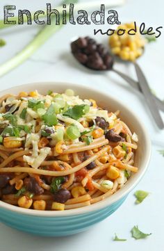 a blue bowl filled with pasta and beans on top of a white table next to spoons