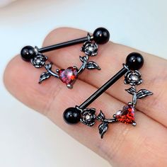 two pairs of black and red piercings on someone's finger with an orange crystal heart in the middle