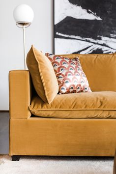 a couch with two pillows on it in front of a large painting and floor lamp