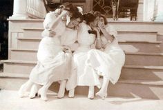 three women in dresses sitting on the steps with their arms around each other's shoulders