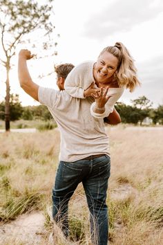 a man holding a woman on his back in the middle of an open field with tall grass