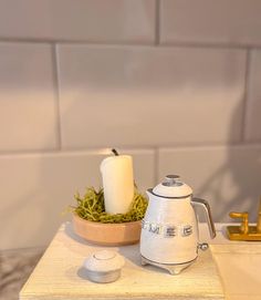 a white coffee pot sitting on top of a wooden table next to a candle holder